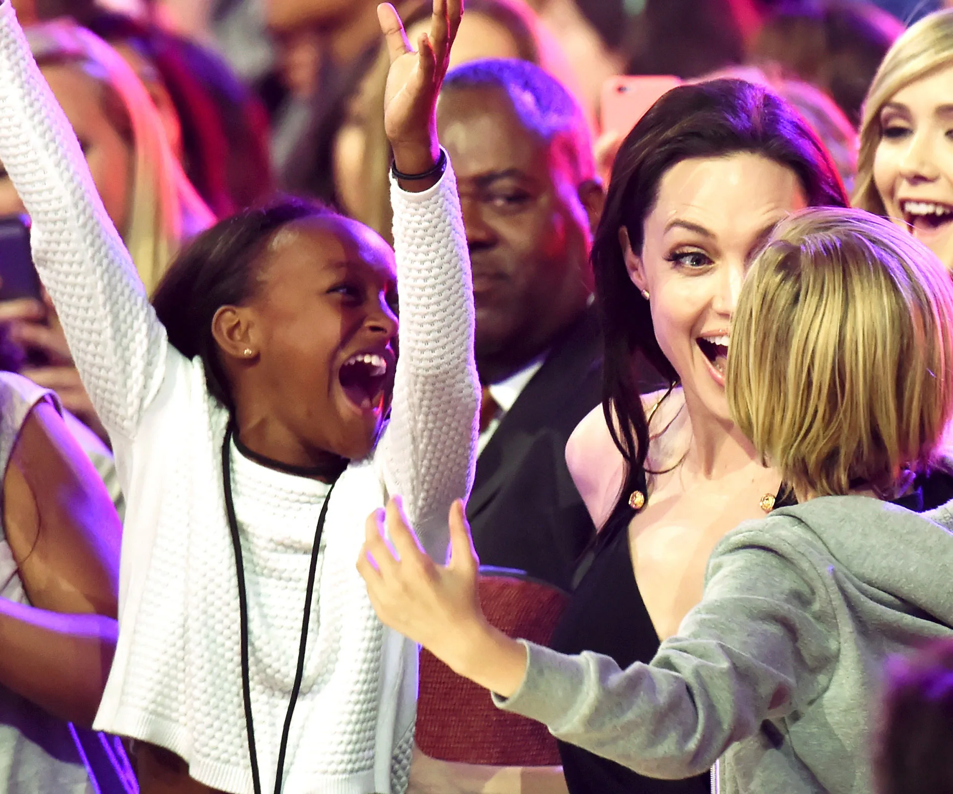 Two children and an adult, all smiling and looking excited at an event with colorful lights.