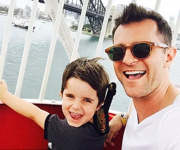 Father and son smiling together on a Ferris wheel by a bridge.