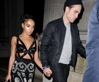 A couple holding hands at night, dressed formally, walking past a stone column.