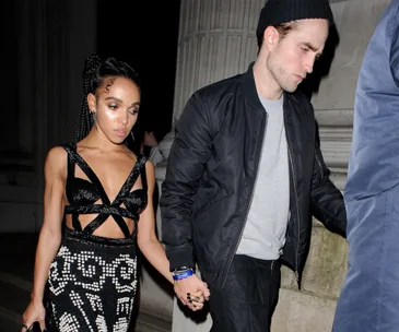 A couple holding hands at night, dressed formally, walking past a stone column.