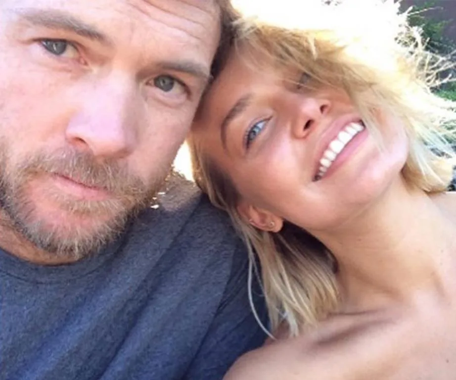 Two people smiling closely together for a selfie, with the sun casting a warm glow on them.