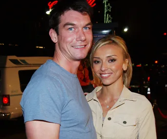 Two people smiling together at an event, with a nighttime background and neon lights.