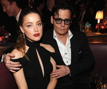 Two people sitting close together at a formal event, one wearing a black outfit and the other a suit with glasses.