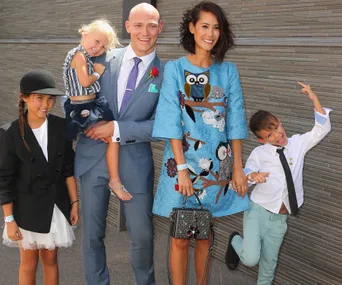 Family posing together, man in blue suit holding child. Woman in blue dress, two other children, all smiling.
