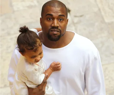 Man holding a small child; both dressed in white outfits, standing outdoors.