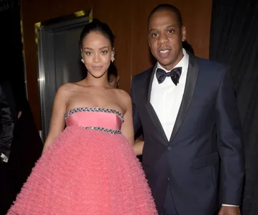 Two people posing together, one in a pink dress and the other in a tuxedo with a bow tie, smiling at a formal event.