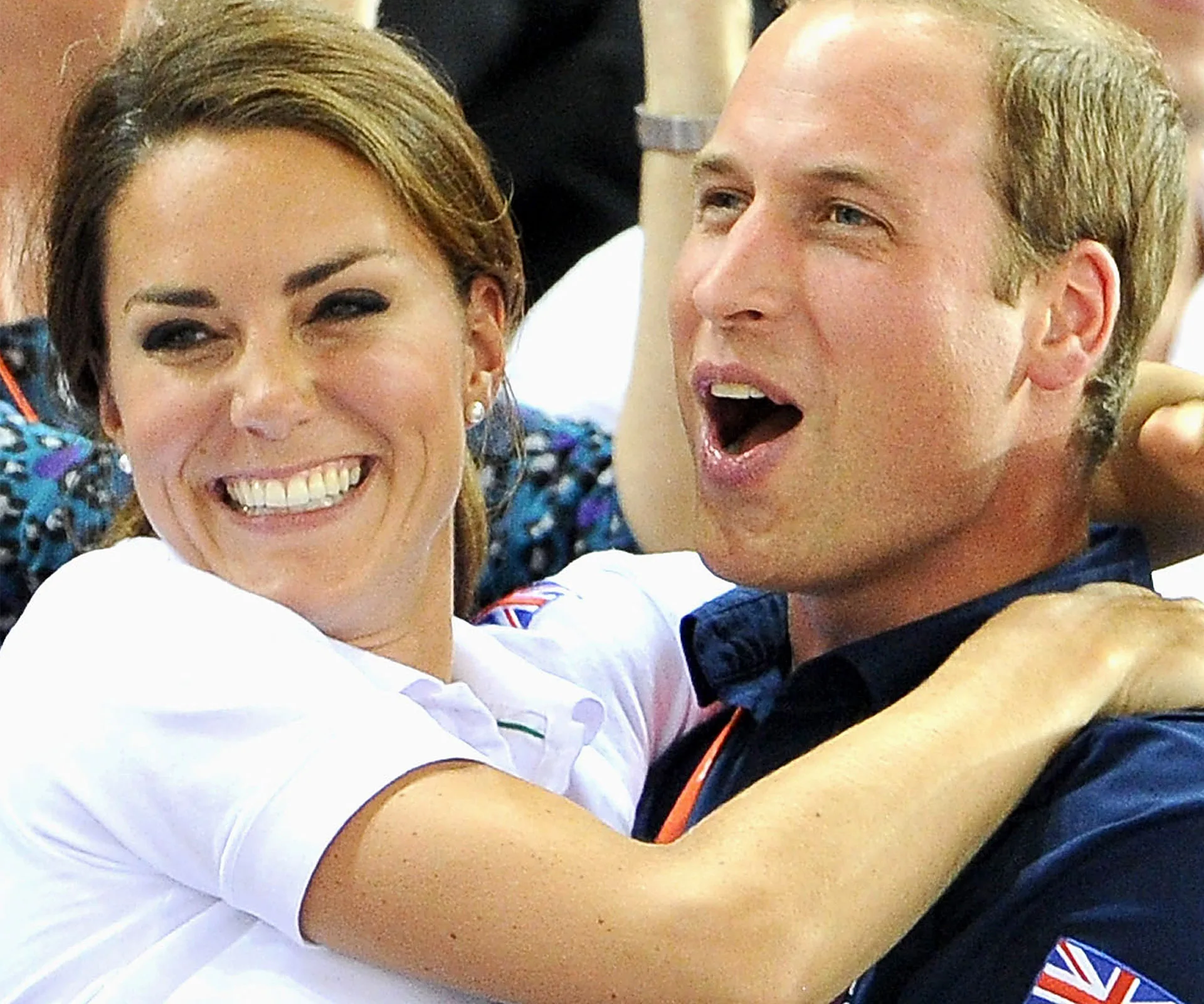 A smiling couple, each wearing a shirt with a British flag, share a joyful moment at a public event.