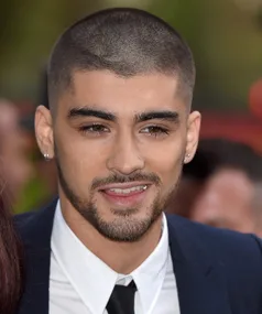 Singer with short hair and beard wearing a suit at a public event, smiling towards the camera.