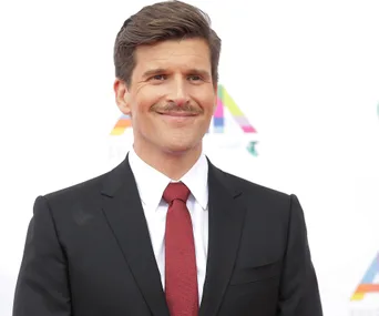 Man in a suit and red tie smiling at a formal event.