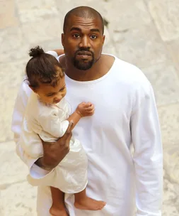 Father holding a young child in a white outfit, standing outdoors on a stone surface.