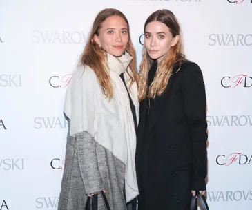 Two women posing together at a fashion event, wearing stylish coats.