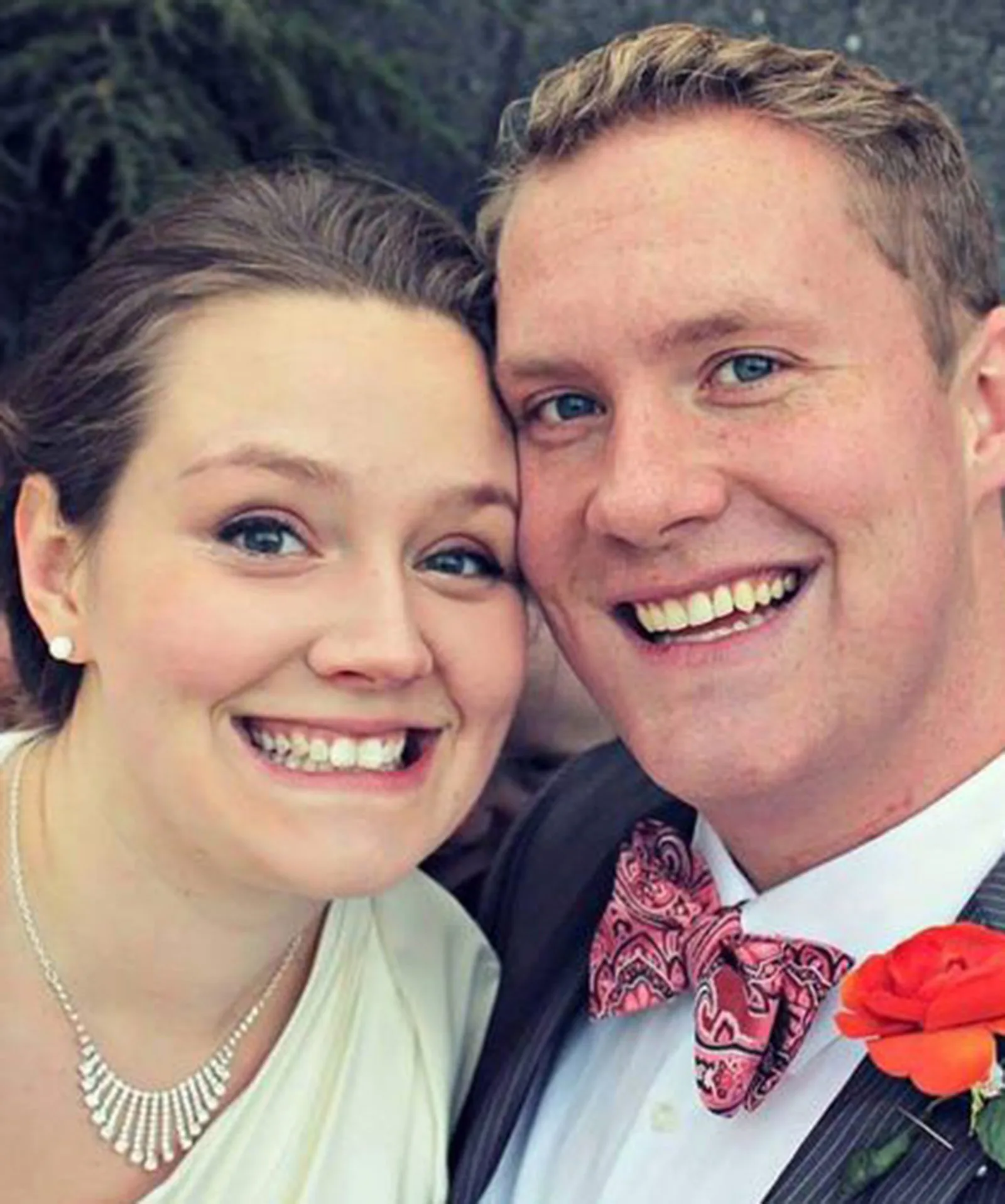 Smiling couple taking a close-up selfie, dressed in wedding attire, outdoors.