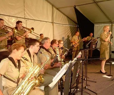 Military band performing with brass instruments and a singer in uniform during an Anzac Day tribute.