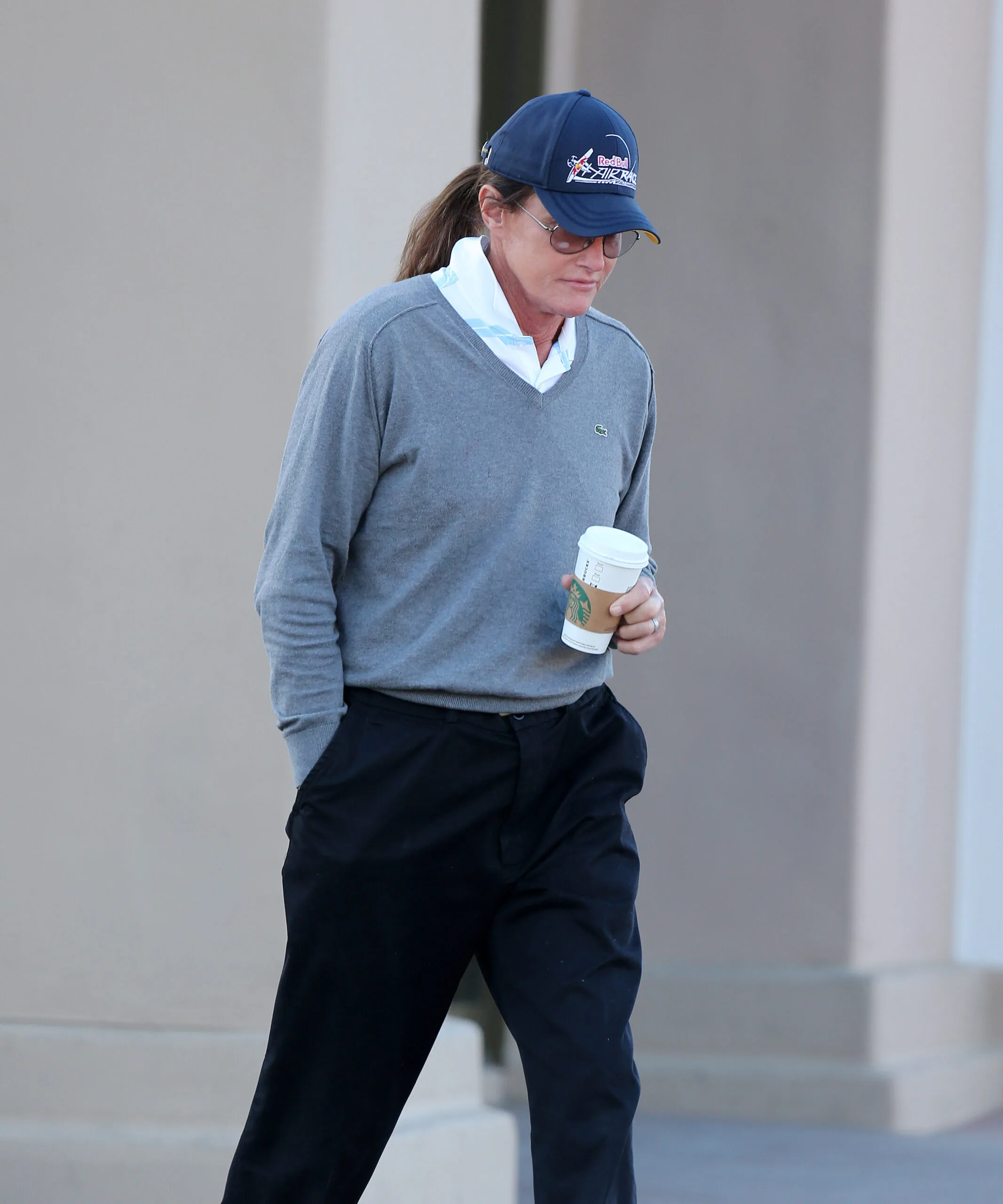 A person in casual attire with a cap holds a coffee cup while walking outdoors.