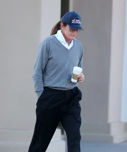A person in casual attire with a cap holds a coffee cup while walking outdoors.