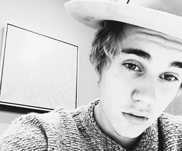 A person wearing a hat and sweater, in a close-up black and white selfie.