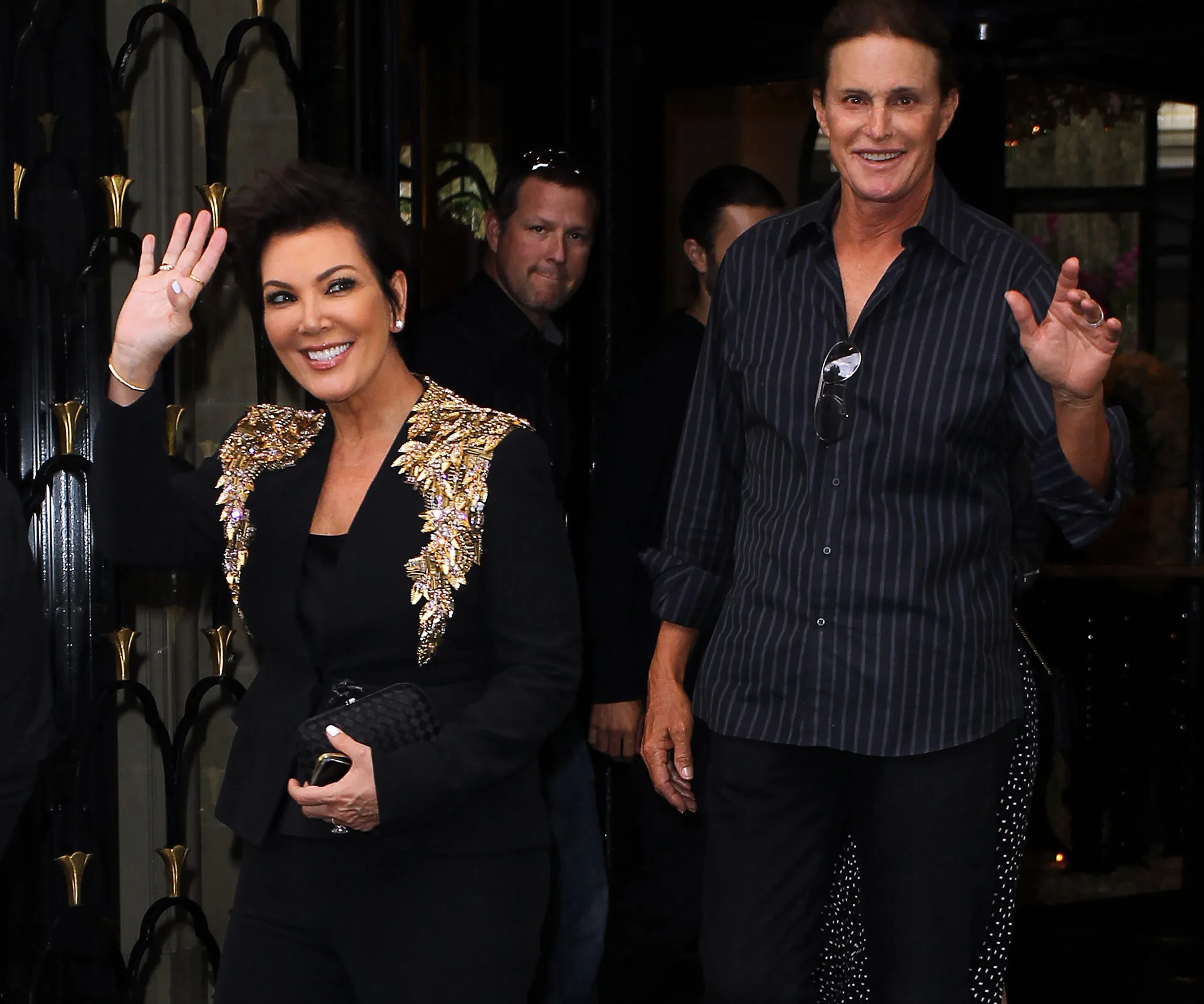 Kris and Bruce Jenner smiling and waving at cameras outside a building.