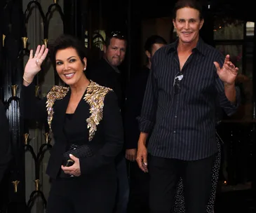 Kris and Bruce Jenner smiling and waving at cameras outside a building.