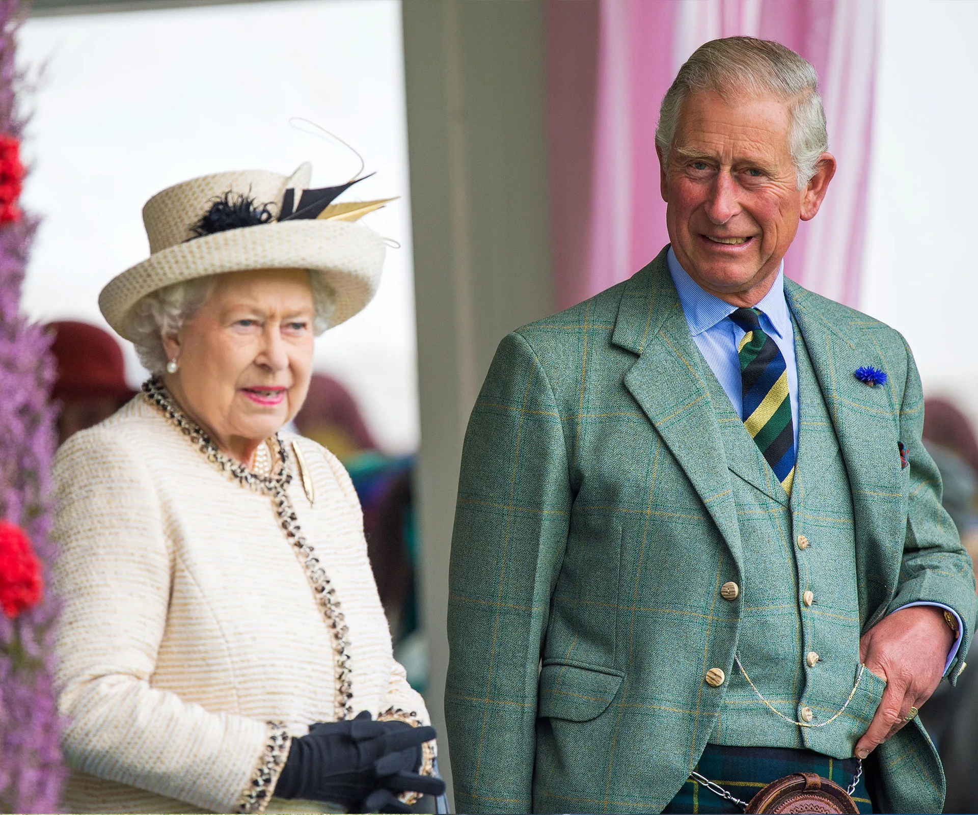 Two elderly individuals in formal attire, one in a light suit with a hat and the other in a green plaid suit, smiling outdoors.