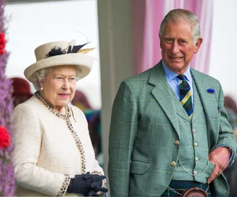 Two elderly individuals in formal attire, one in a light suit with a hat and the other in a green plaid suit, smiling outdoors.