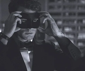 Man in a tuxedo putting on a black masquerade mask, scene from "Fifty Shades Darker".