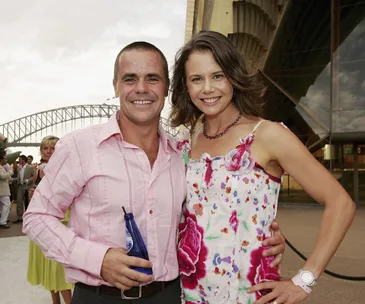 Two people smiling at an outdoor event with the Sydney Harbour Bridge in the background.