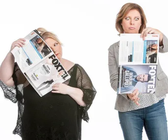 Two women with surprised expressions, holding Foxtel magazines, pose humorously against a white background.