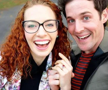 Couple smiling at the camera, woman showing engagement ring, celebrating their engagement.