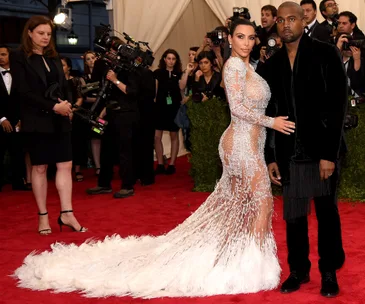 A couple poses on the red carpet at the 2015 Met Gala, with the woman in a sheer, feathered dress and the man in a black suit.