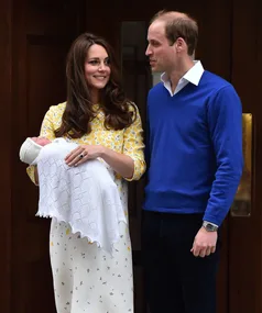 "Couple smiling outside hospital with newborn baby wrapped in a white blanket."