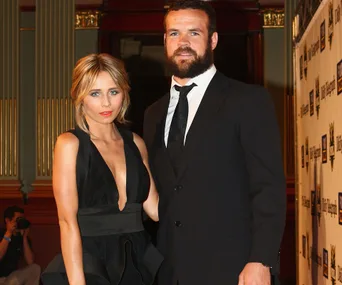 A woman in a black dress stands beside a man in a suit at an event, posing for a photo.