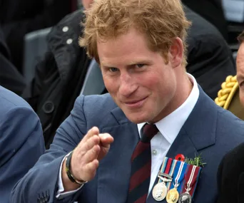 A man in a suit with medals on his chest gestures, smiling warmly.