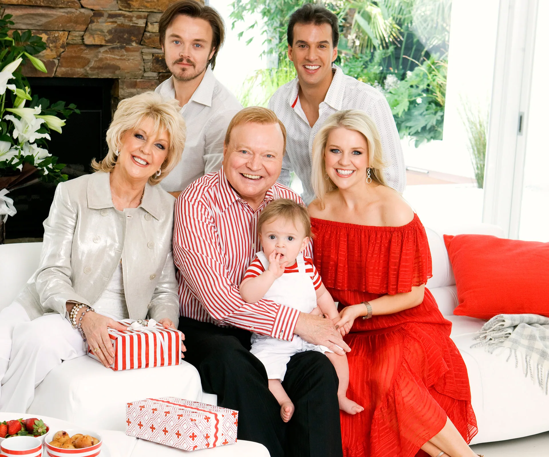 A family gathered on a white couch, wearing coordinating red and white outfits, with gifts and smiling expressions.