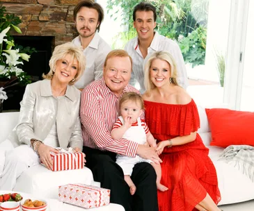 A family gathered on a white couch, wearing coordinating red and white outfits, with gifts and smiling expressions.