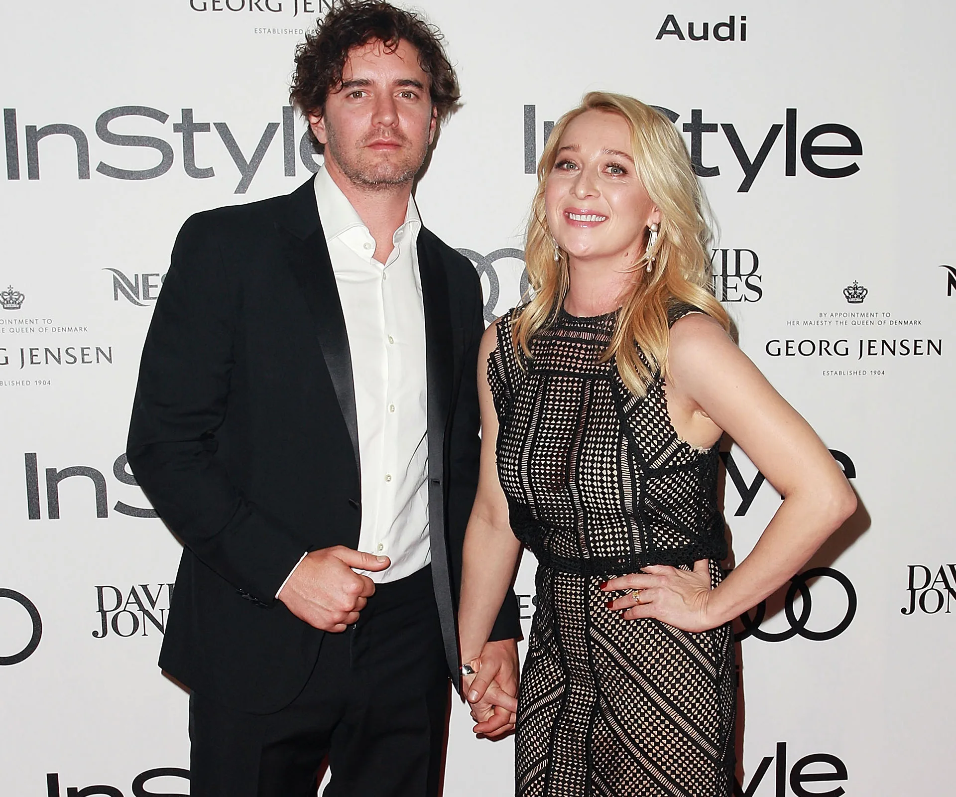 Couple dressed in formal attire, holding hands at an InStyle magazine event backdrop.