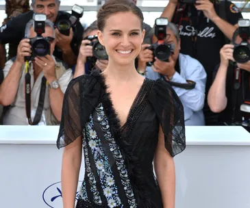 Woman in a black floral dress on the red carpet at the 2015 Cannes Film Festival, surrounded by photographers.