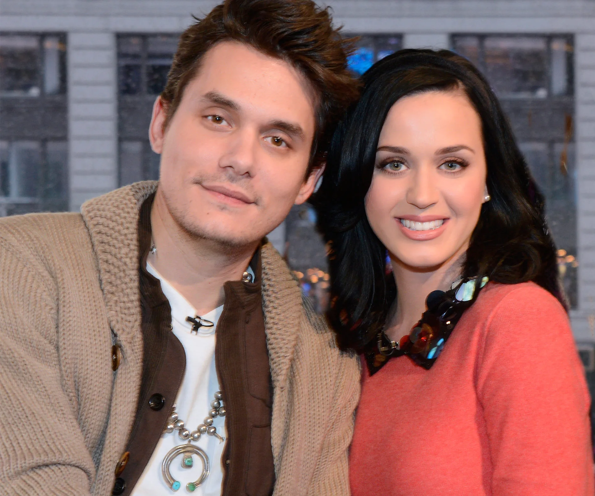 Two people smiling together indoors, with one wearing a necklace and the other in a pink top.