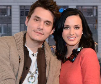 Two people smiling together indoors, with one wearing a necklace and the other in a pink top.