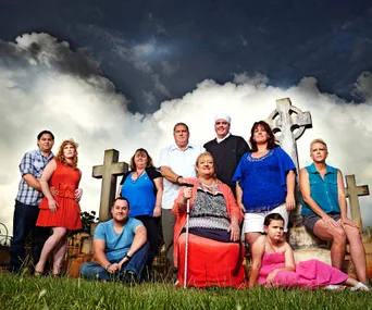 Group of people posing in front of gravestones under a dramatic cloudy sky.