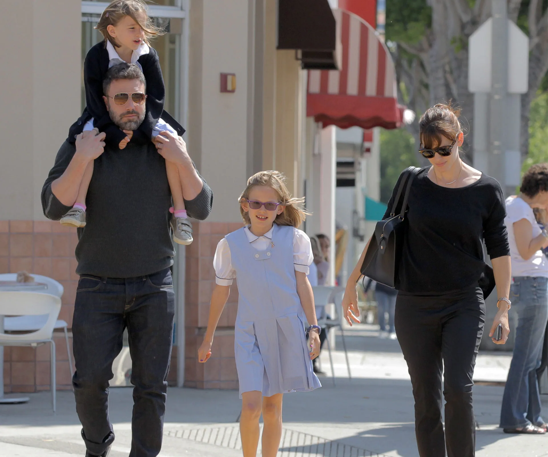 Family walking together outside, Ben carrying a child on his shoulders, Jennifer walking beside another child.