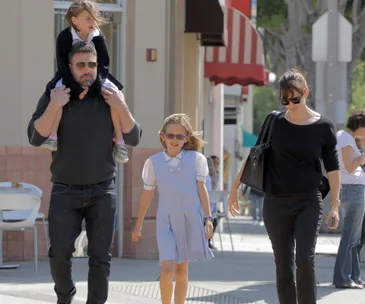 Family walking together outside, Ben carrying a child on his shoulders, Jennifer walking beside another child.
