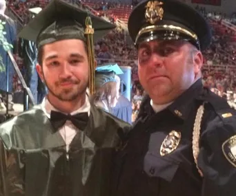 Graduating student poses with a supportive police officer at a ceremony.