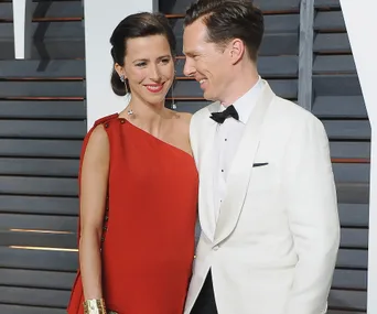 A couple in formal attire, the man in a white tuxedo, and the woman in a red dress, smiling at each other.