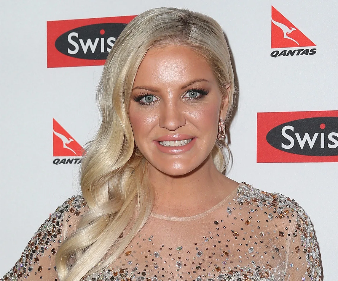Blonde woman in a sparkly dress smiles at an event; Swisse and Qantas logos in the background.