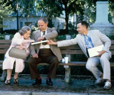 Forrest Gump sharing chocolates with strangers on a park bench.