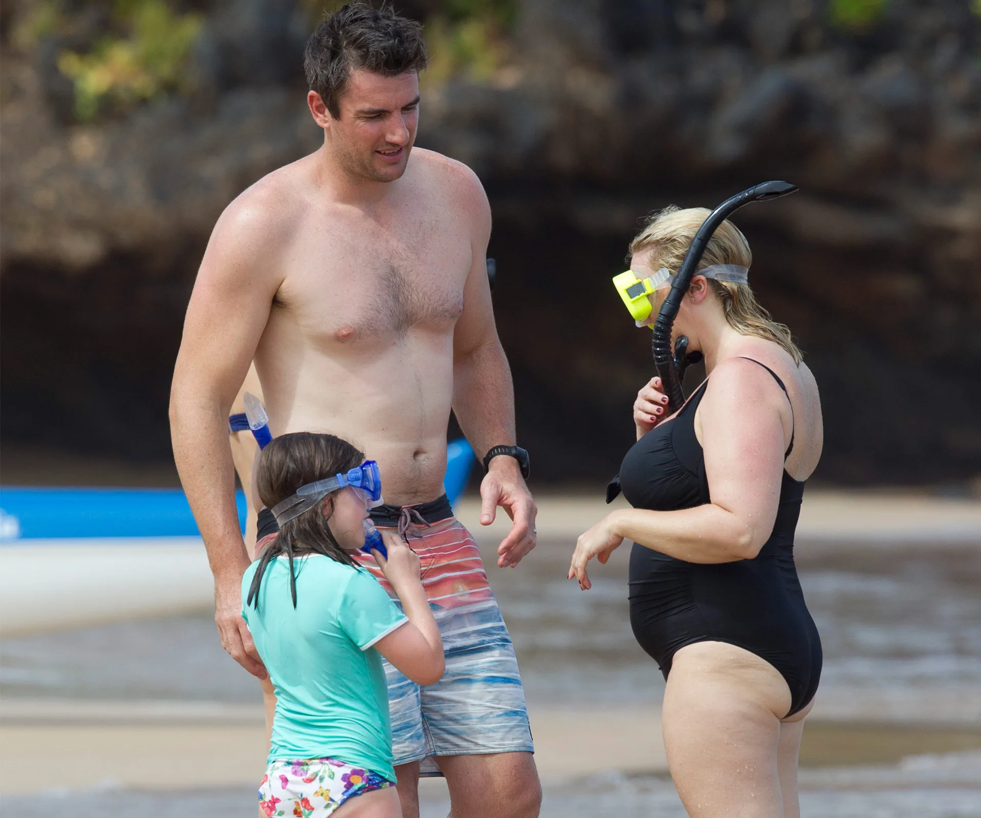 A family enjoying snorkeling on a sandy beach in Hawaii, preparing their gear.