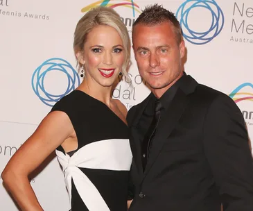 "Couple smiling in formal attire at a tennis awards event, posing in front of a step-and-repeat banner."