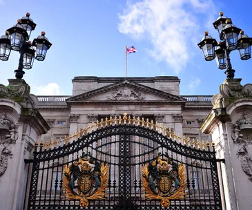 Buckingham Palace with ornate gates and a Union Jack flag flying atop the building.