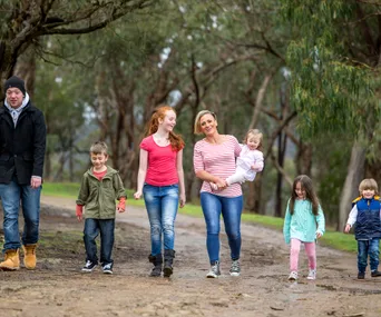 Family walking outdoors on a forest path, with children and adults smiling and enjoying nature.