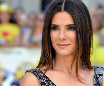 Sandra Bullock at an outdoor event, smiling slightly, with blurred crowd in the background.